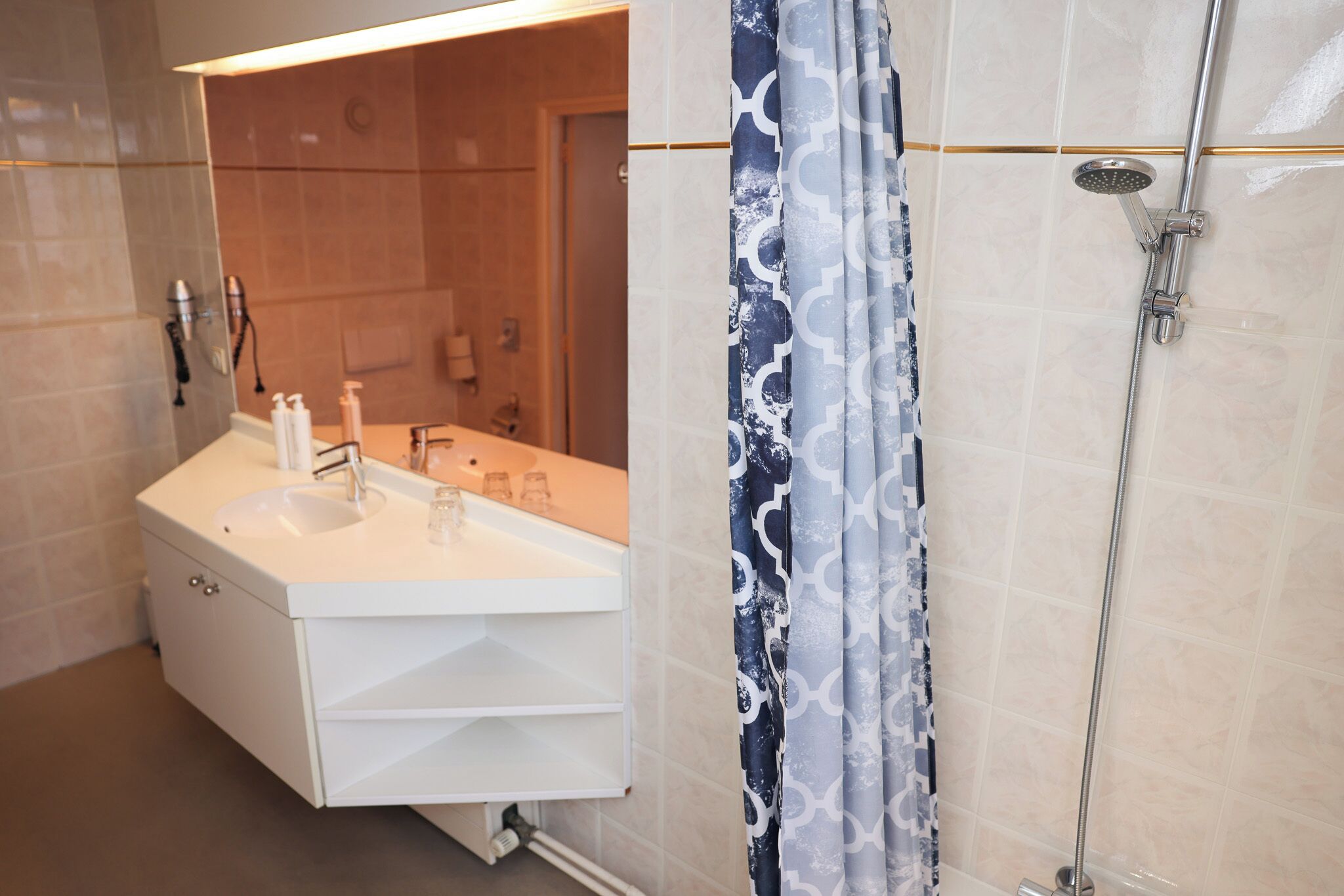 Un baño moderno con tocador blanco, ducha con cabezal de ducha manual y cortina estampada.