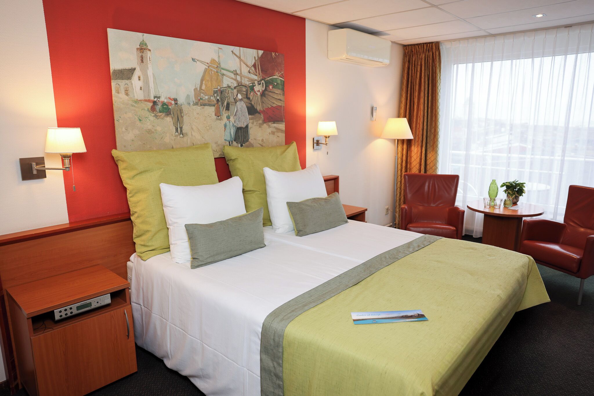 Habitación de hotel con una cama grande, dos mesitas de noche, una pequeña mesa con sillas, un cuadro en la pared y una ventana con cortinas.