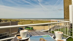 A balcony with a view of the beach, a table with a menu, and two cups of coffee. - Hotel Noordzee (Katwijk Aan Zee)