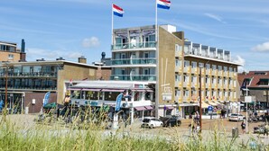A hotel with a modern design, featuring a prominent balcony and flags. - Hotel Noordzee (Katwijk Aan Zee)