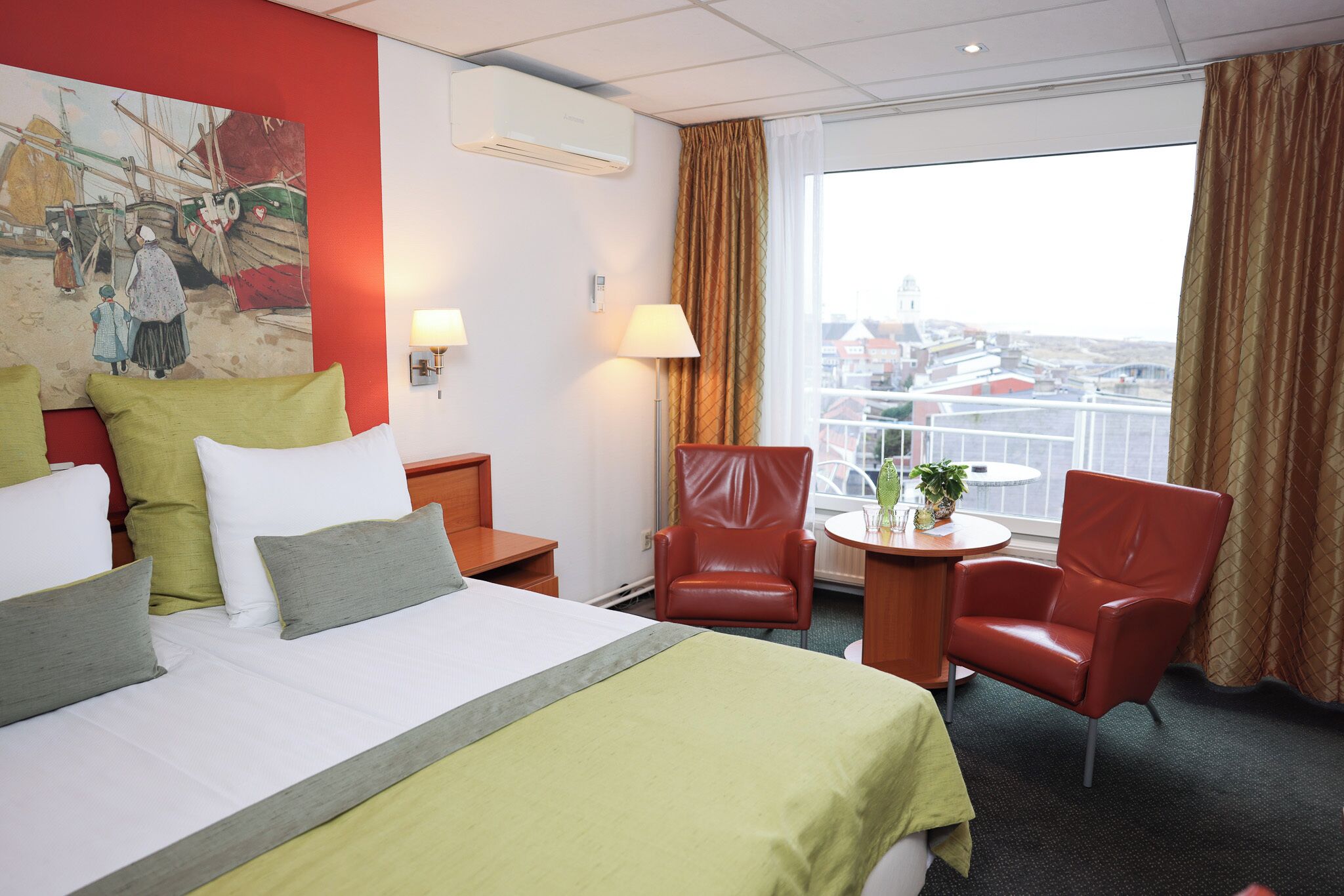 A hotel room with a bed, two chairs, a desk, a lamp, and a painting on the wall.