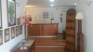 Un espace d’accueil avec un comptoir en bois, des tableaux encadrés aux murs, un vase rempli de fleurs et une lampe.