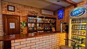 Un espace bar avec un comptoir en briques, des étagères remplies de bouteilles, une horloge et un réfrigérateur contenant des boissons en bouteille.