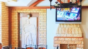 L’intérieur d’un restaurant avec des murs en briques, une cheminée en pierre et un téléviseur fixé au-dessus de la cheminée.