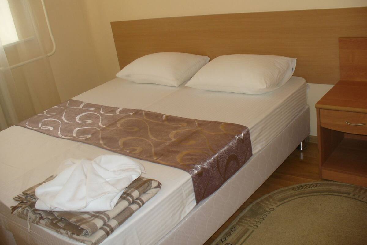 A neatly made bed with a brown patterned bedspread, white pillows, and a white blanket folded at the foot of the bed.