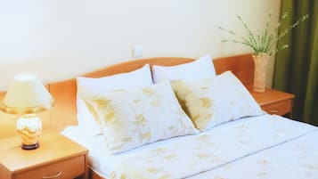 Una cama bien hecha con ropa de cama estampada con motivos florales, una lámpara de noche y un jarrón con una planta sobre la mesita de noche.