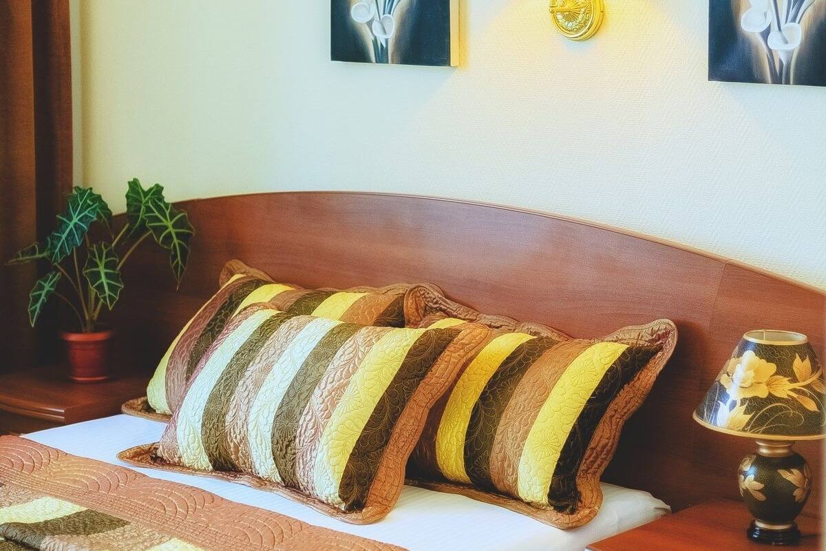 A hotel room with a bed, a nightstand, a lamp, a potted plant, and wall art.