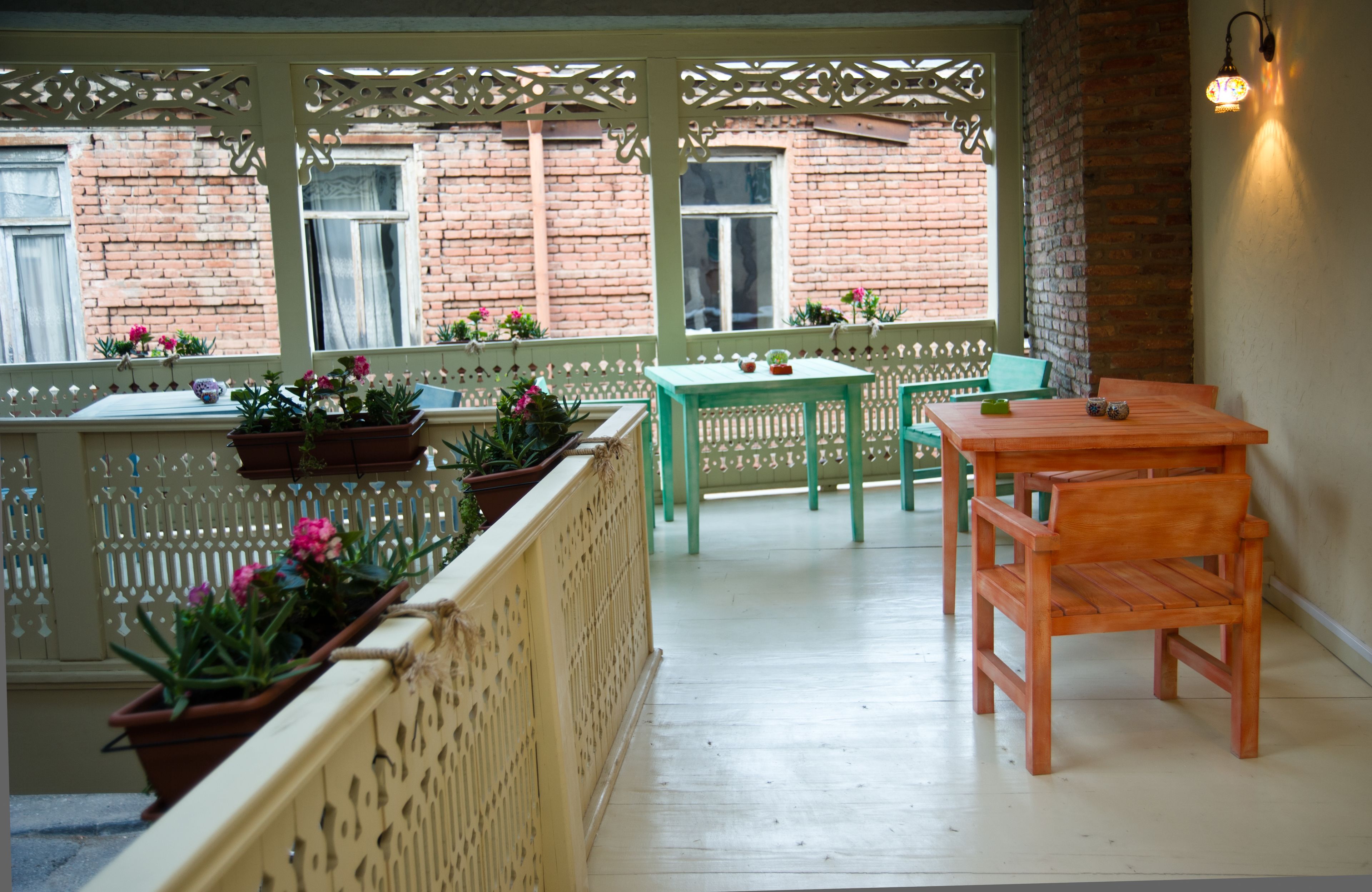 A balcony with a wooden table and chairs, potted plants, and a view of a brick building.
