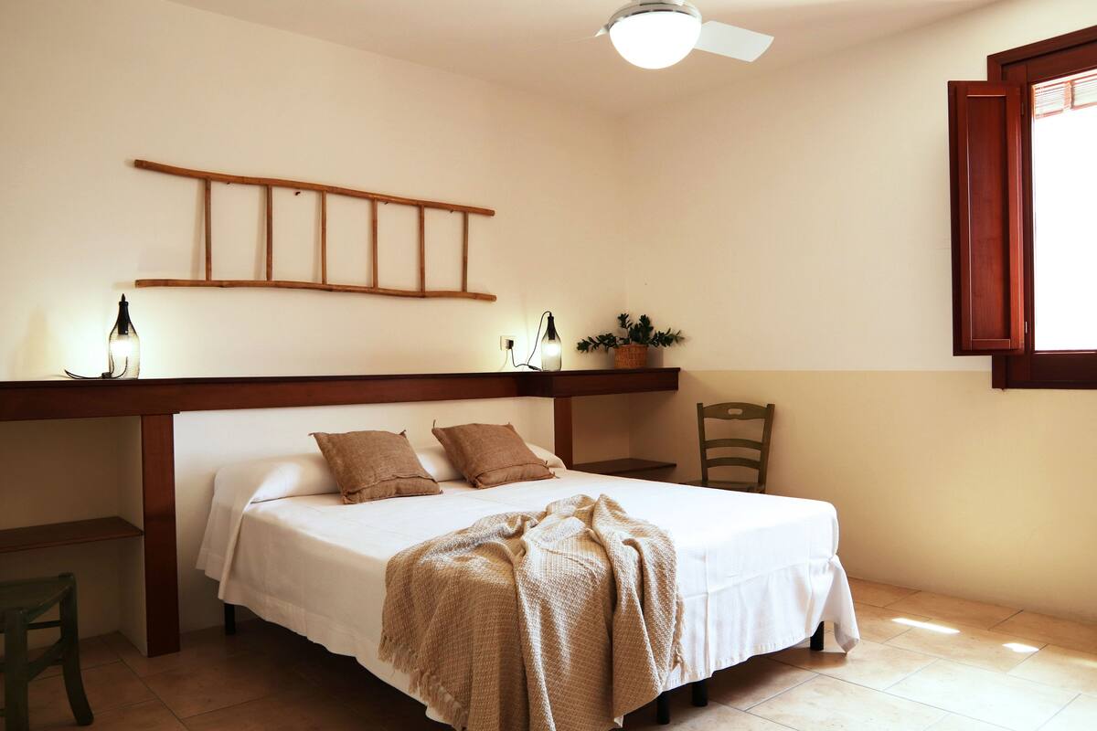 Une chambre à coucher comprenant un lit, un bureau, une chaise, un ventilateur de plafond et une fenêtre.