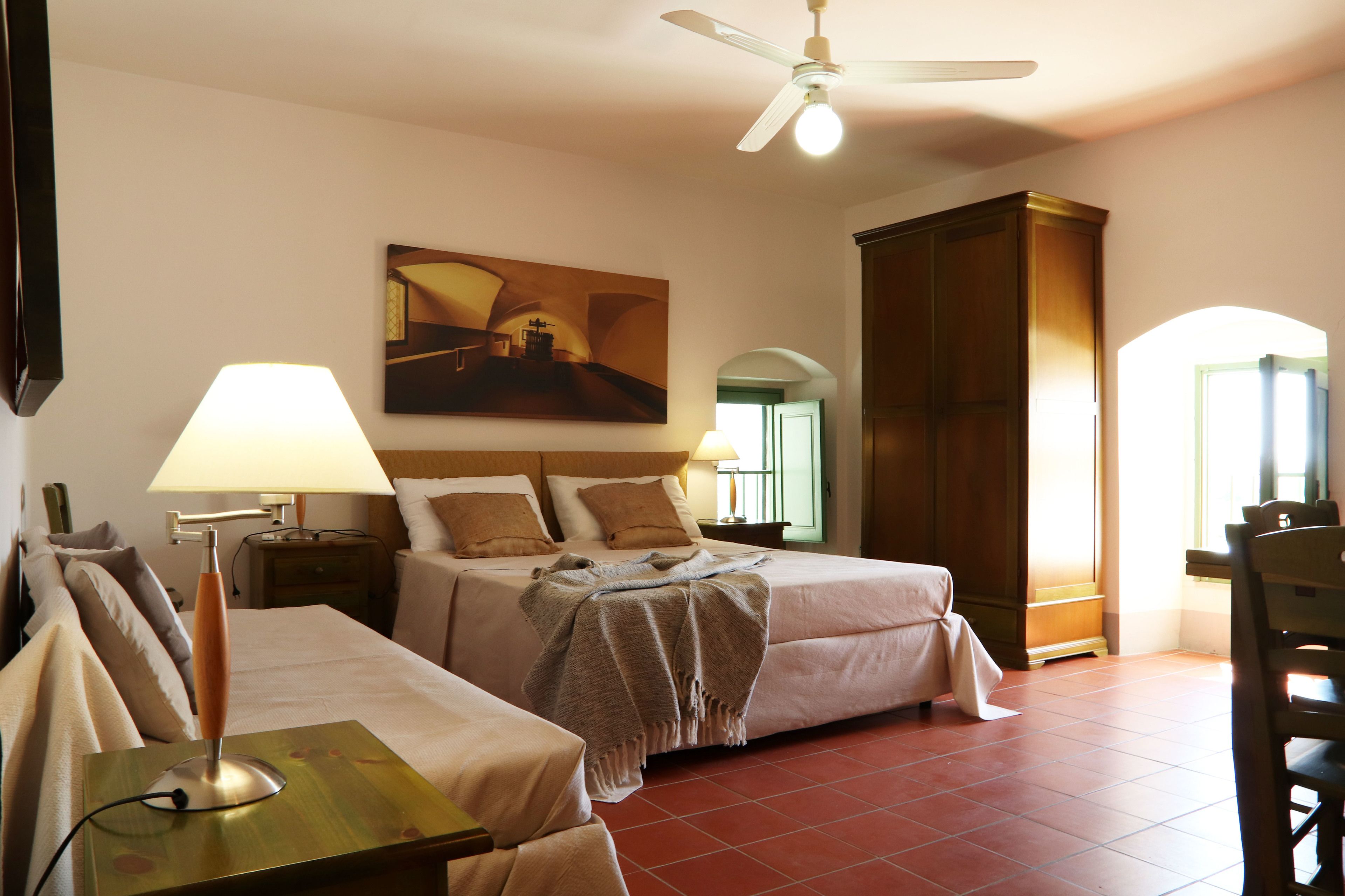 Una camera d'albergo con un letto, una scrivania, una lampada, una ventola a soffitto e un quadro appeso al muro.