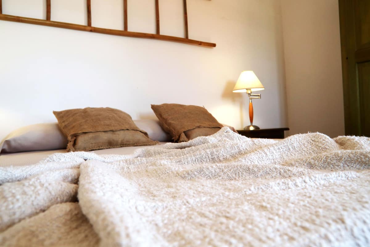 Un lit avec une couverture blanche et deux oreillers marron, une table de chevet avec une lampe et une tête de lit en bois.