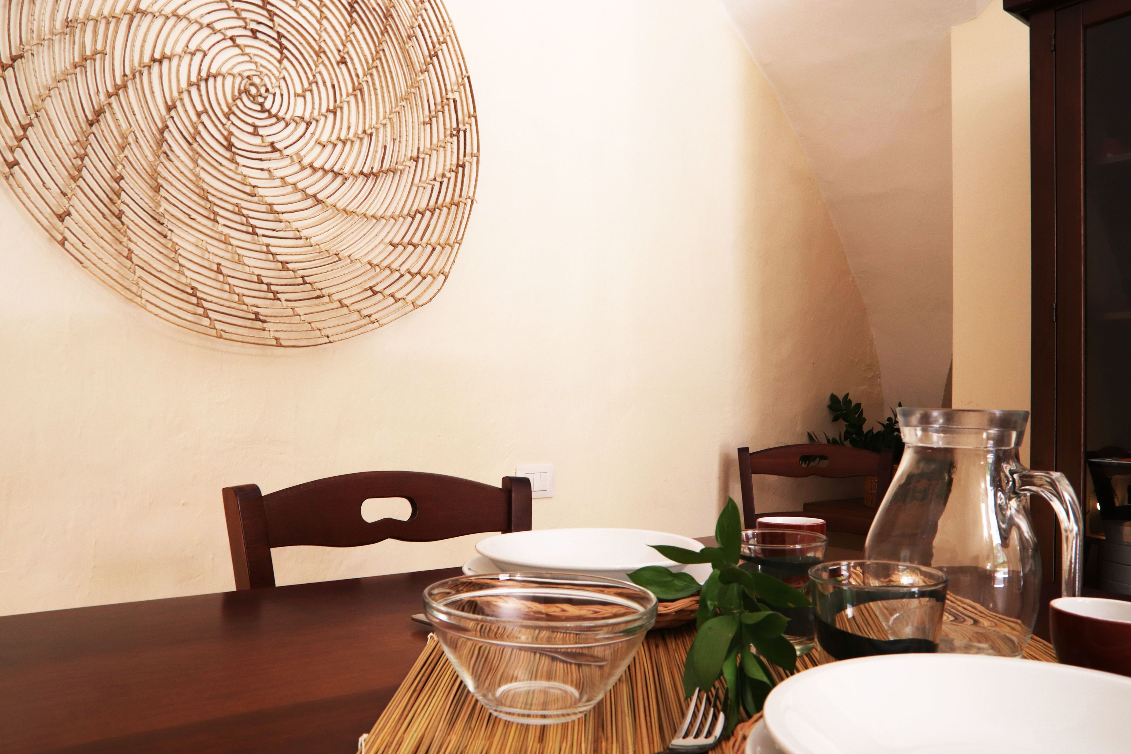 A dining table with a woven placemat, a pitcher, a glass bowl, and a plate.