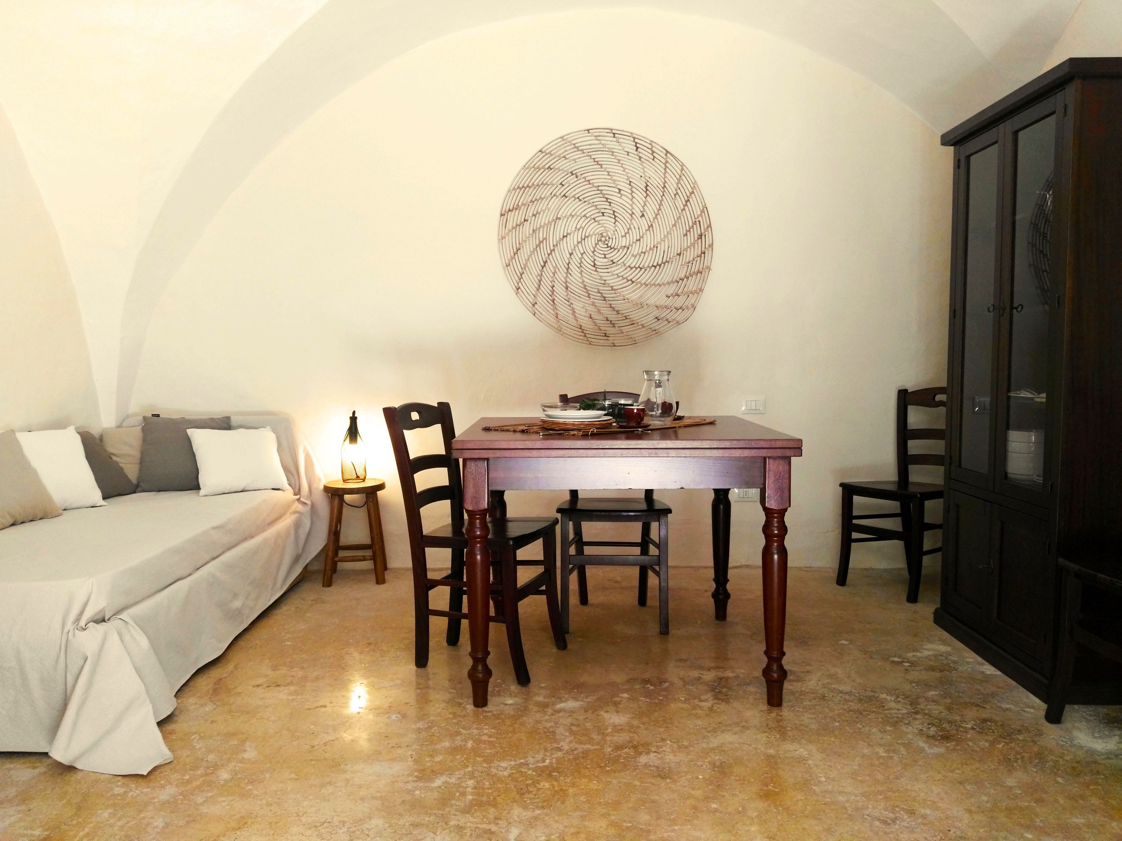 Una habitación acogedora con cama, una mesa de comedor y sillas. Se observa un mueble aparador y una obra de arte en la pared sobre la mesa.