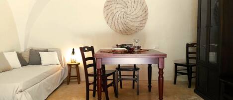 Una habitación acogedora con cama, una mesa de comedor y sillas. Se observa un mueble aparador y una obra de arte en la pared sobre la mesa.