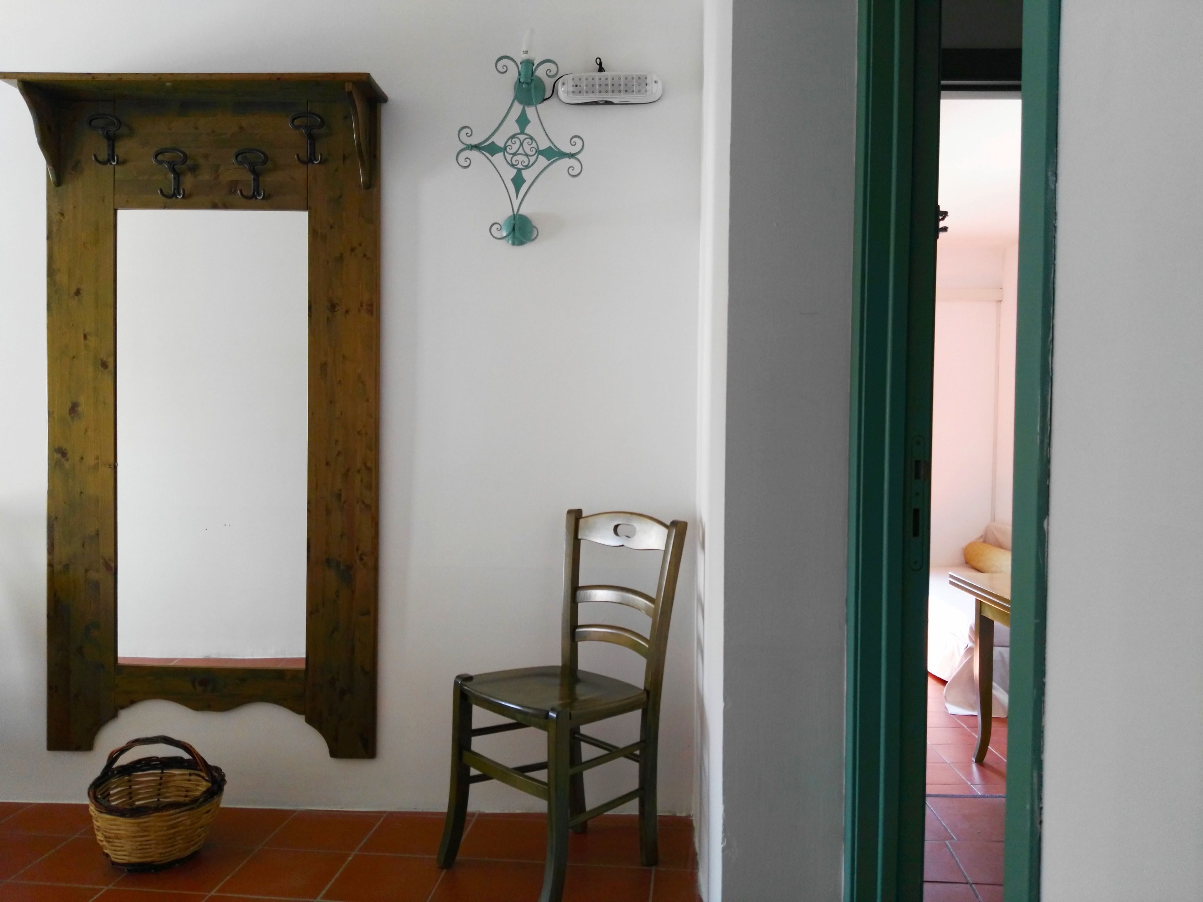 Une pièce comprenant un porte-manteau en bois, un élément de décoration murale en métal vert, un panier en osier et une chaise en bois.