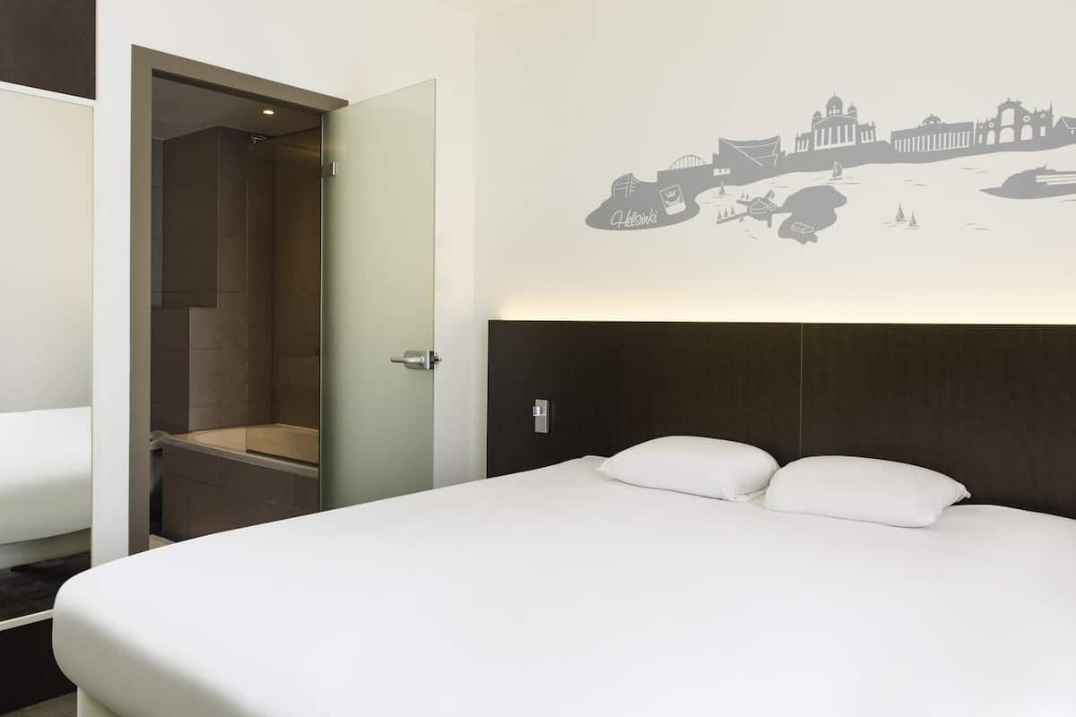 A hotel room with a bed, a shower, and a cityscape mural on the wall.
