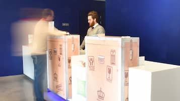 Un espace d’accueil avec un mur bleu et un comptoir d’accueil blanc. On y trouve trois boîtes de rangement étiquetées, par exemple, avec les mots « FRAGILE » et « CE CÔTÉ VERS LE HAUT ».