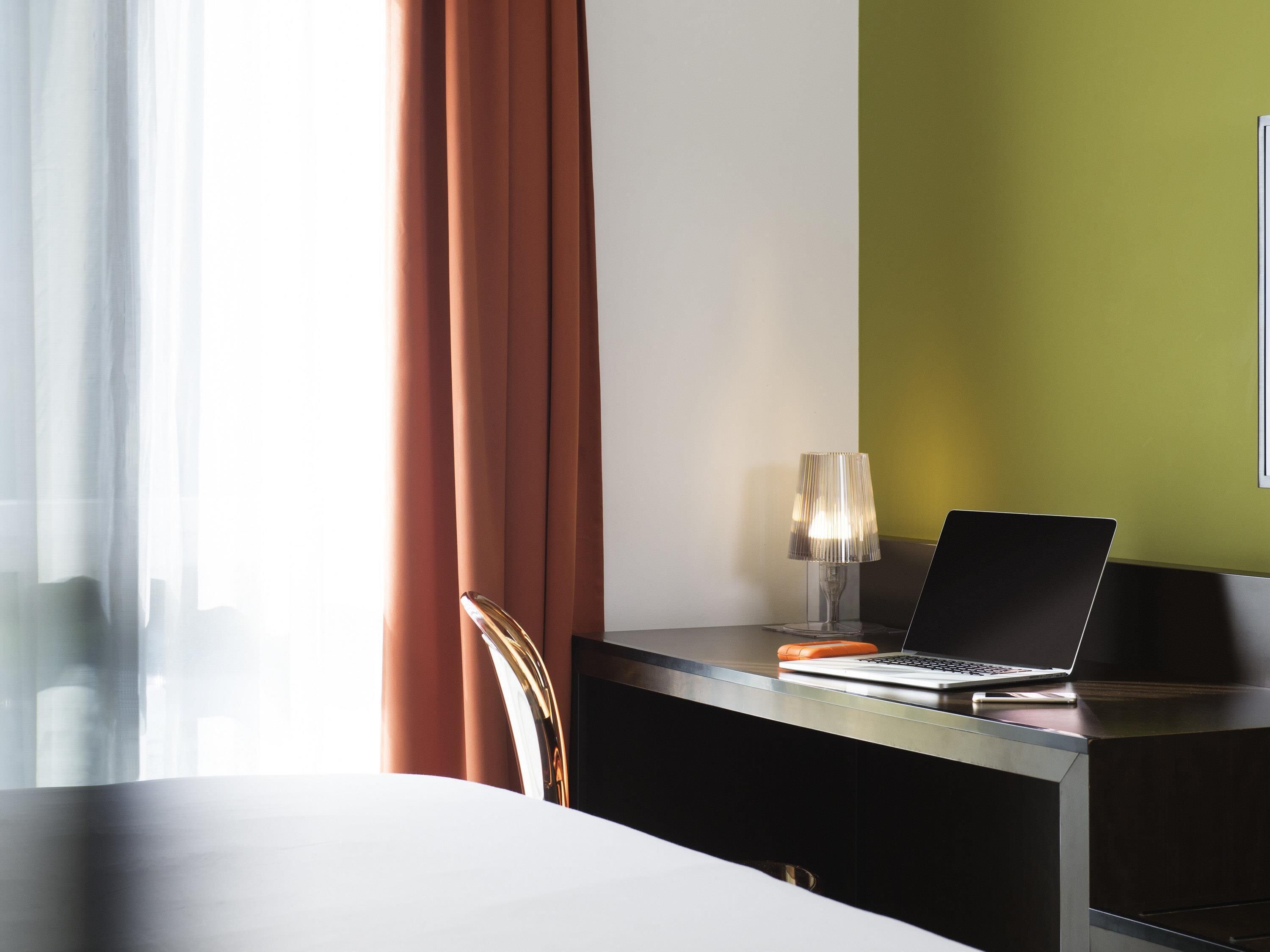 Una habitación de hotel con cama, escritorio, ordenador portátil, lámpara y silla.
