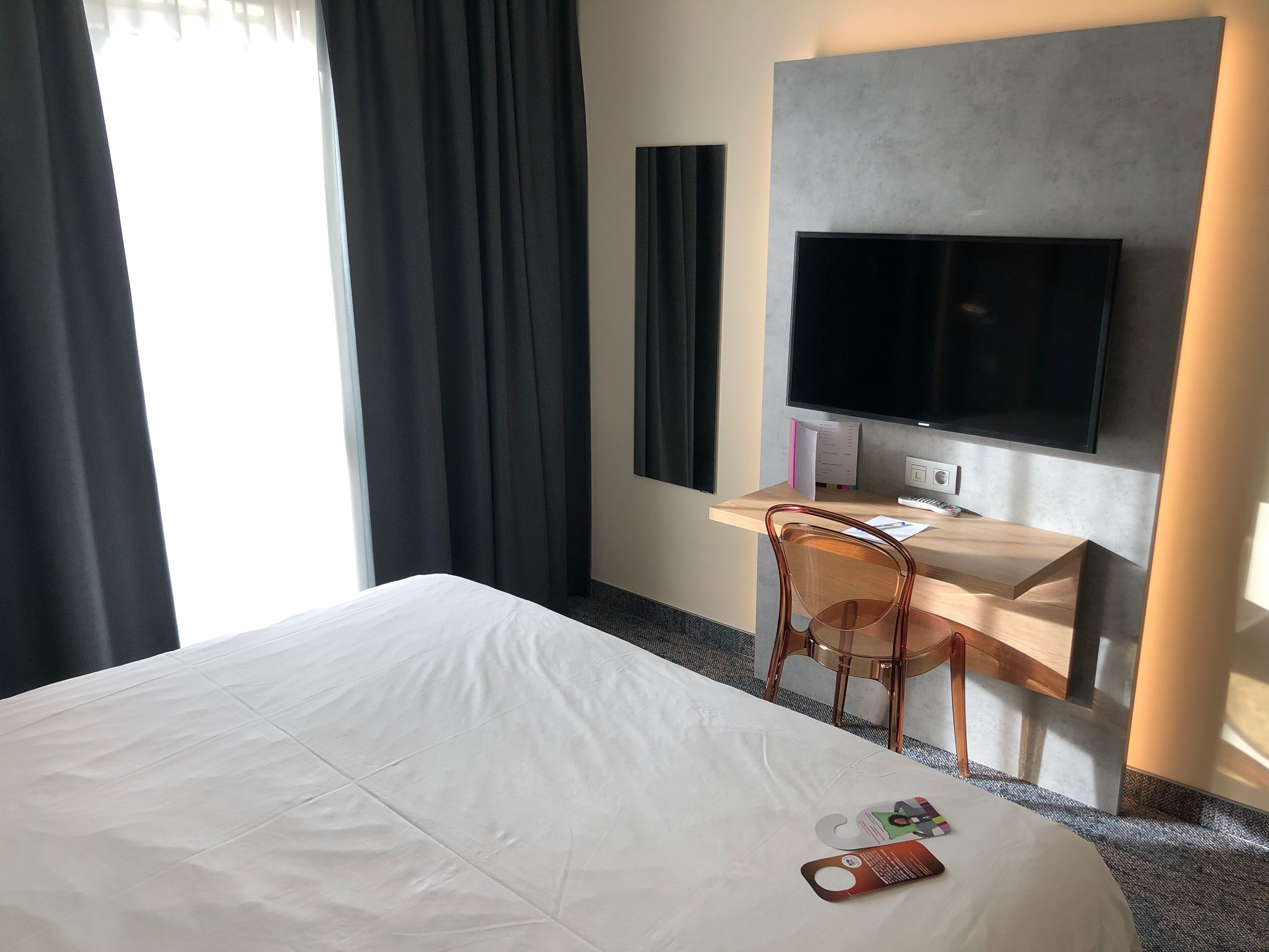 A hotel room with a large bed, a desk with a computer, a chair, and a TV mounted on the wall.