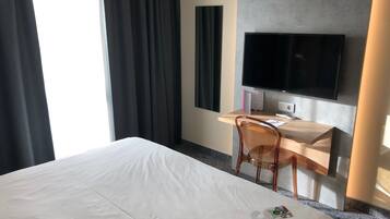 A hotel room with a large bed, a desk with a computer, a chair, and a TV mounted on the wall.