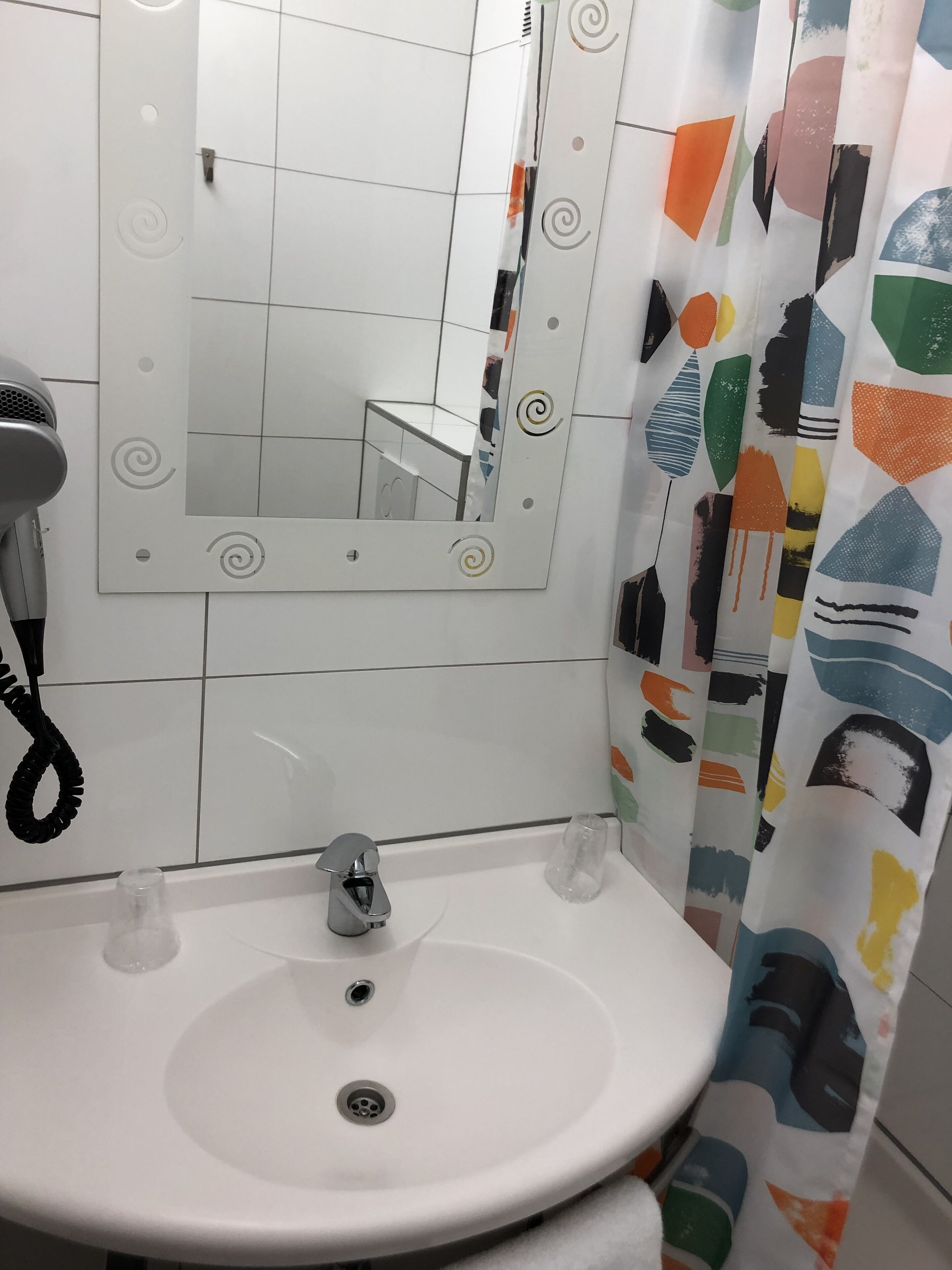 Une salle de bain avec un lavabo blanc, un miroir orné de motifs décoratifs en spirale et un rideau de douche aux motifs abstraits.