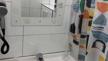 Une salle de bain avec un lavabo blanc, un miroir orné de motifs décoratifs en spirale et un rideau de douche aux motifs abstraits.