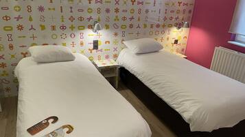 A room with two single beds, a small table, a wall clock, and a radiator.