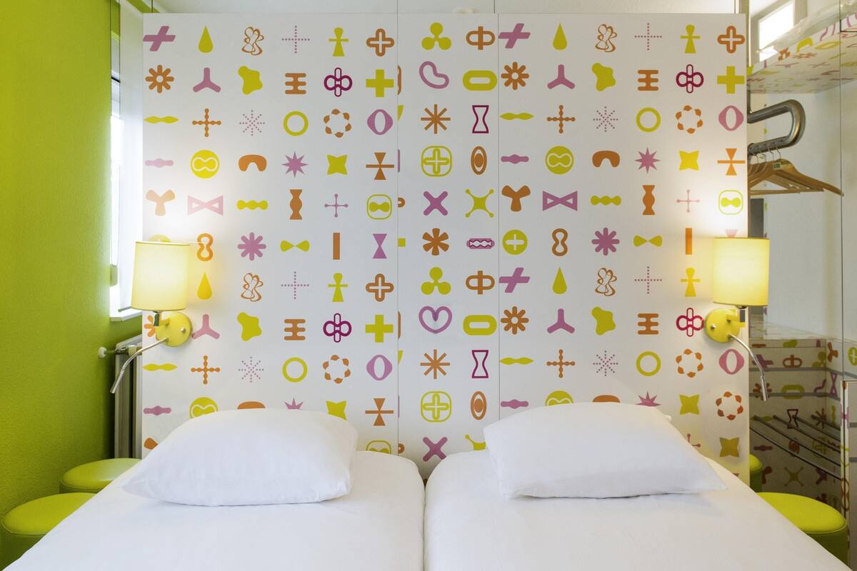 A room with two beds, green walls, and a patterned wallpaper.