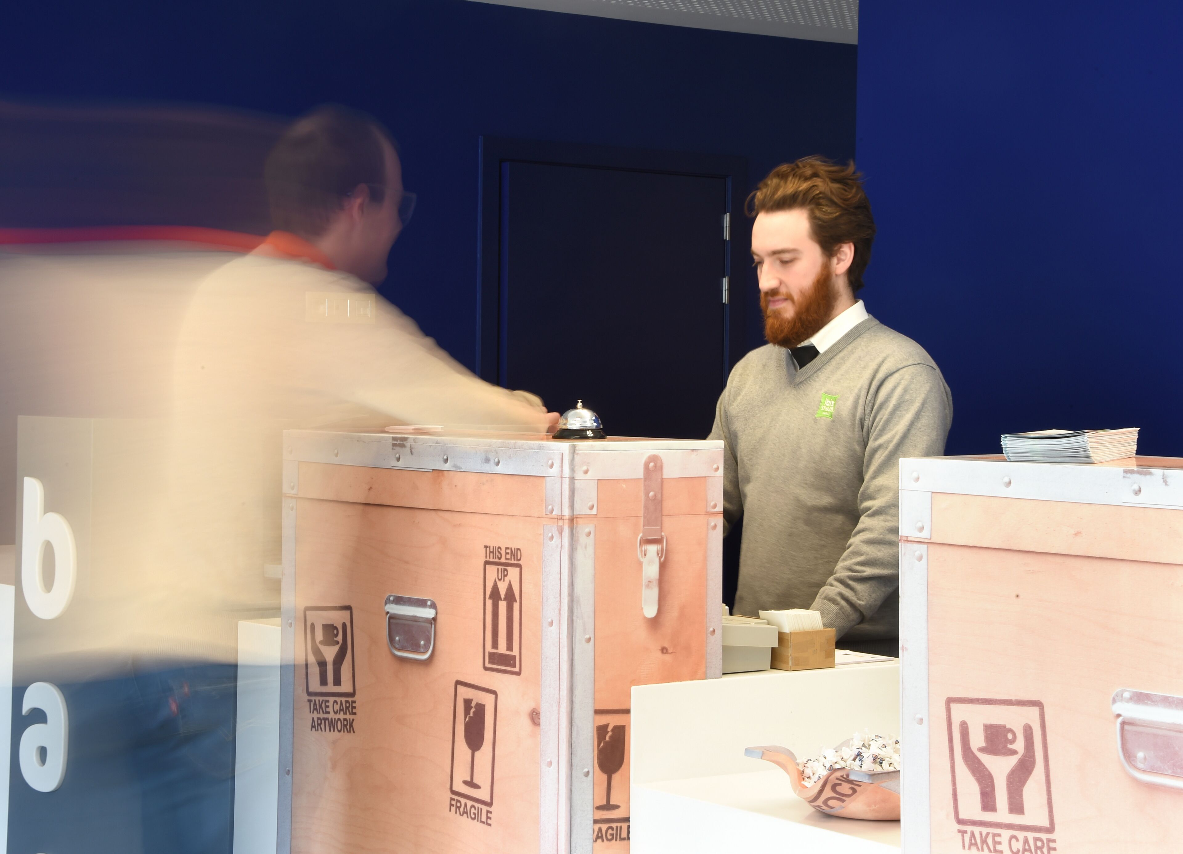 Un homme se tient devant un comptoir, à côté de cartons étiquetés « Œuvres d’art : à manipuler avec précaution » et « Fragile ».