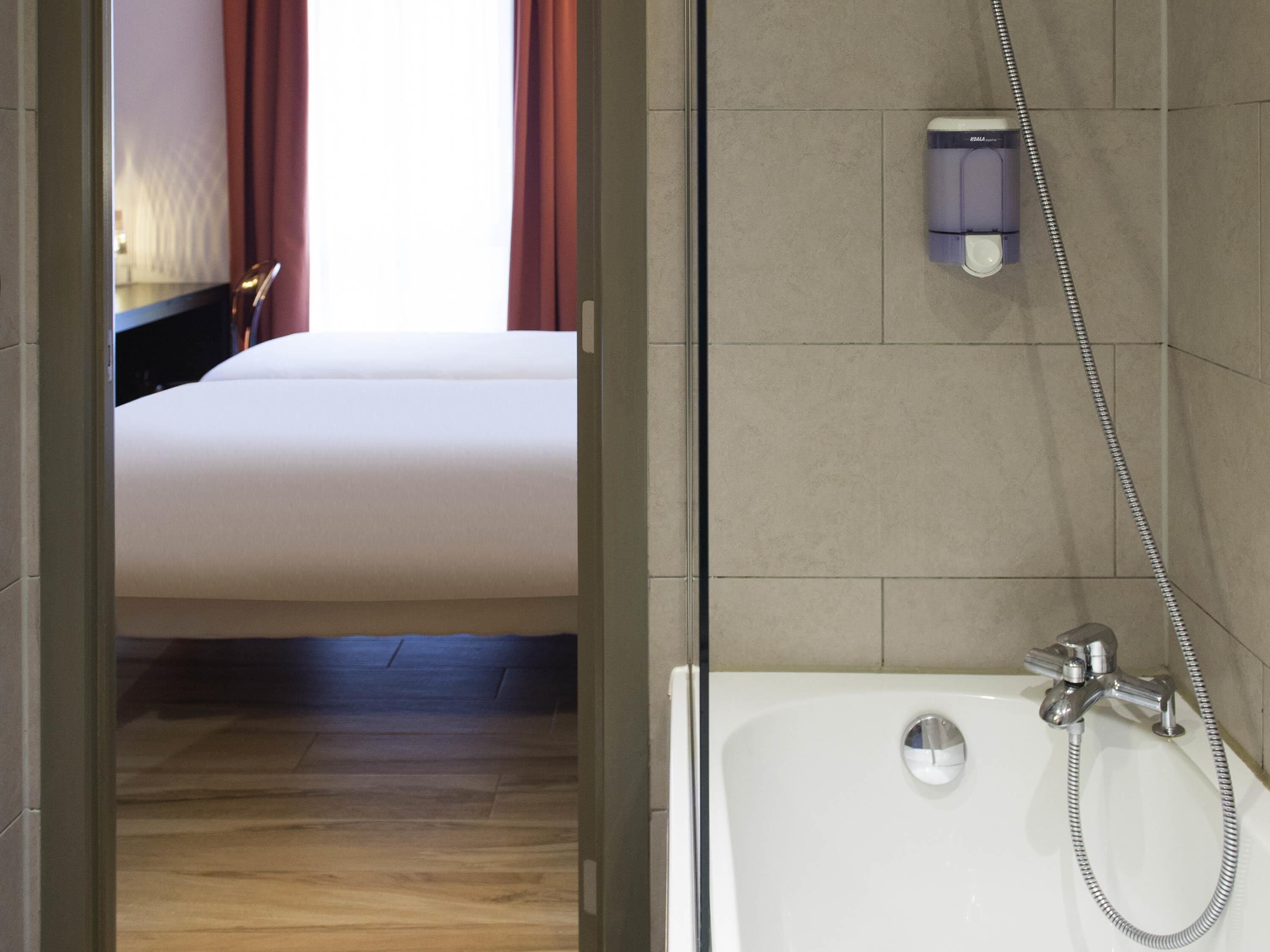 A hotel room with a bed, a shower, and a mirror.