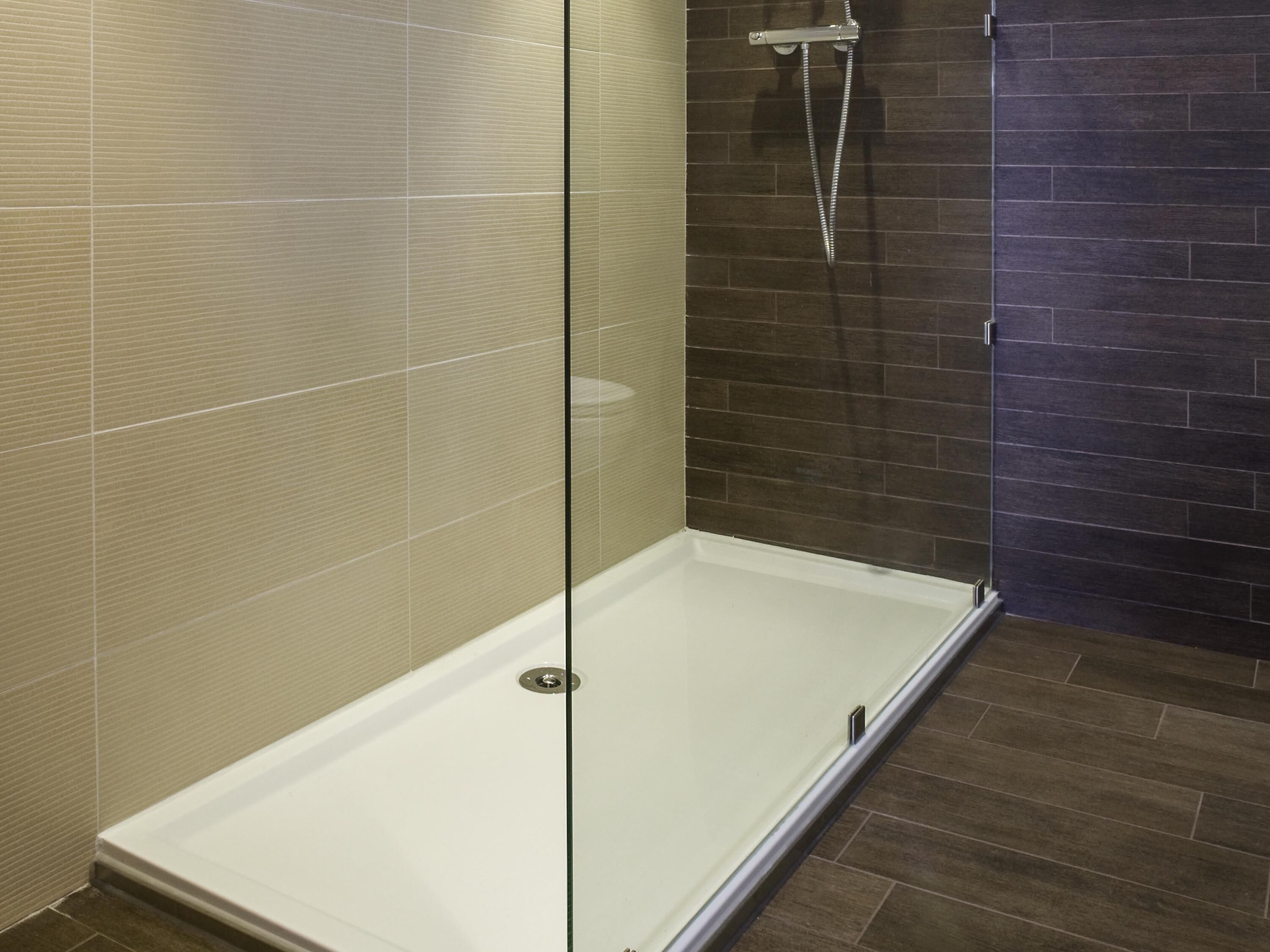 A glass-enclosed shower stall with a dark tiled wall and a wooden floor.