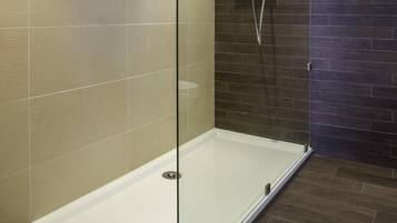 A glass-enclosed shower stall with a dark tiled wall and a wooden floor.