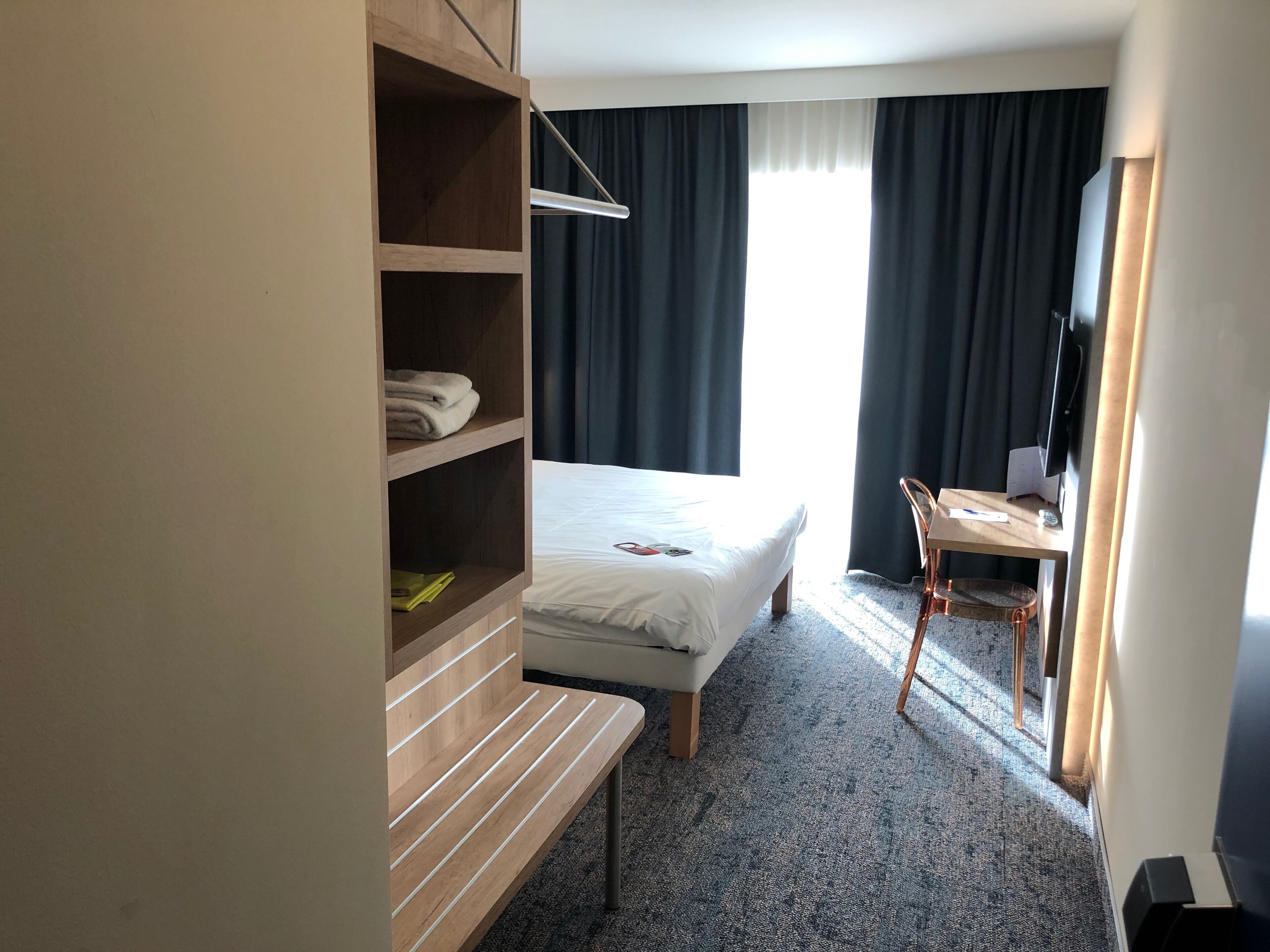 Een hotelkamer met een bed, een bureau, een stoel, een televisie en een kledingkast.