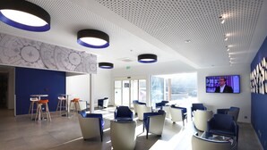 Un espace d’attente moderne avec des chaises bleues et blanches, un comptoir d’accueil et un grand écran de télévision.