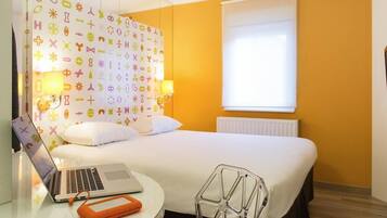 Ein Hotelzimmer mit einem Bett, einem Schreibtisch mit einem Laptop, einem Stuhl und einer Wand mit verschiedenen Symbolen.