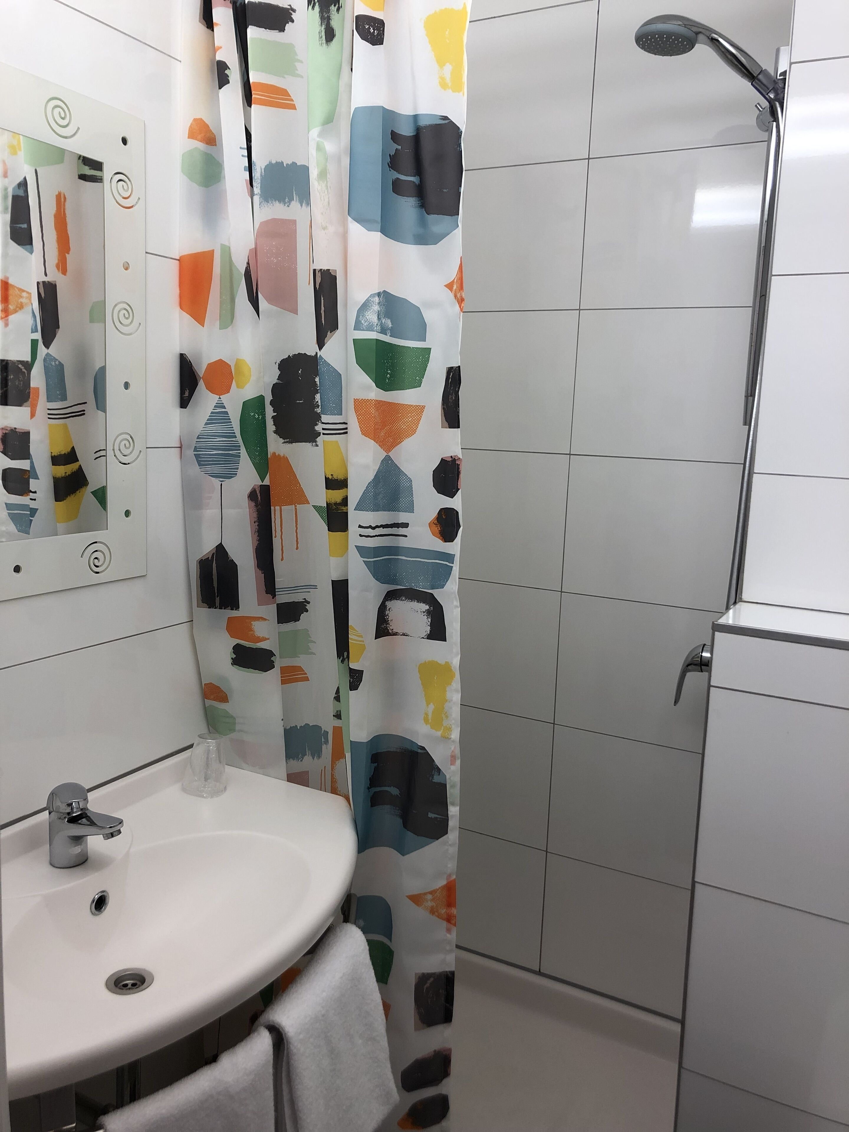A bathroom with a white sink, a mirror, a shower with a modern design, and a colorful shower curtain.