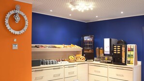 Un espace réservé au petit-déjeuner, avec un buffet, des machines à café et une horloge au mur.