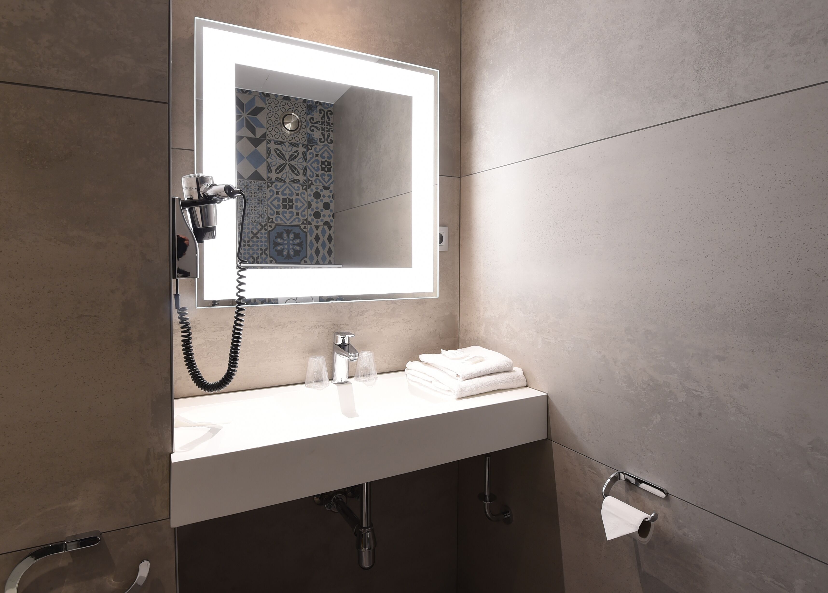 Un baño moderno con un lavabo blanco, un espejo, un perchero para toallas y un dispensador de papel higiénico.