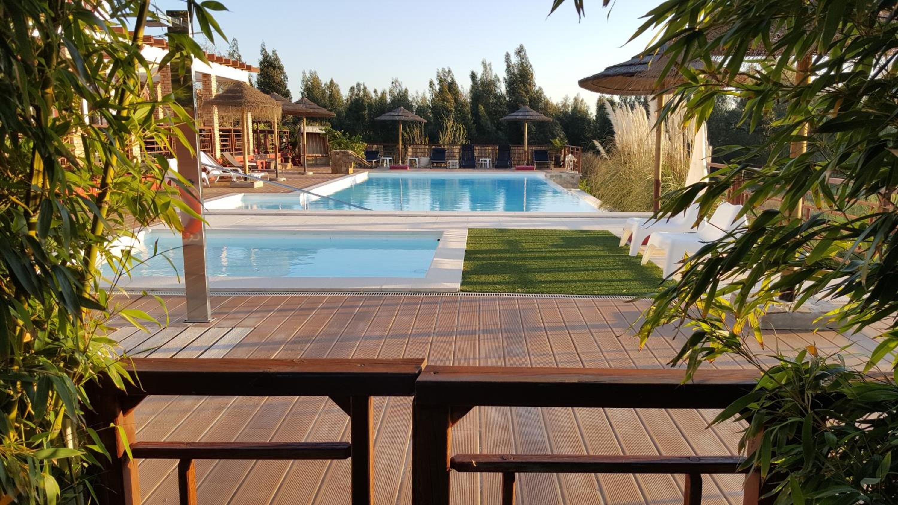 A pool area with a wooden deck, lounge chairs, and a small grassy area.