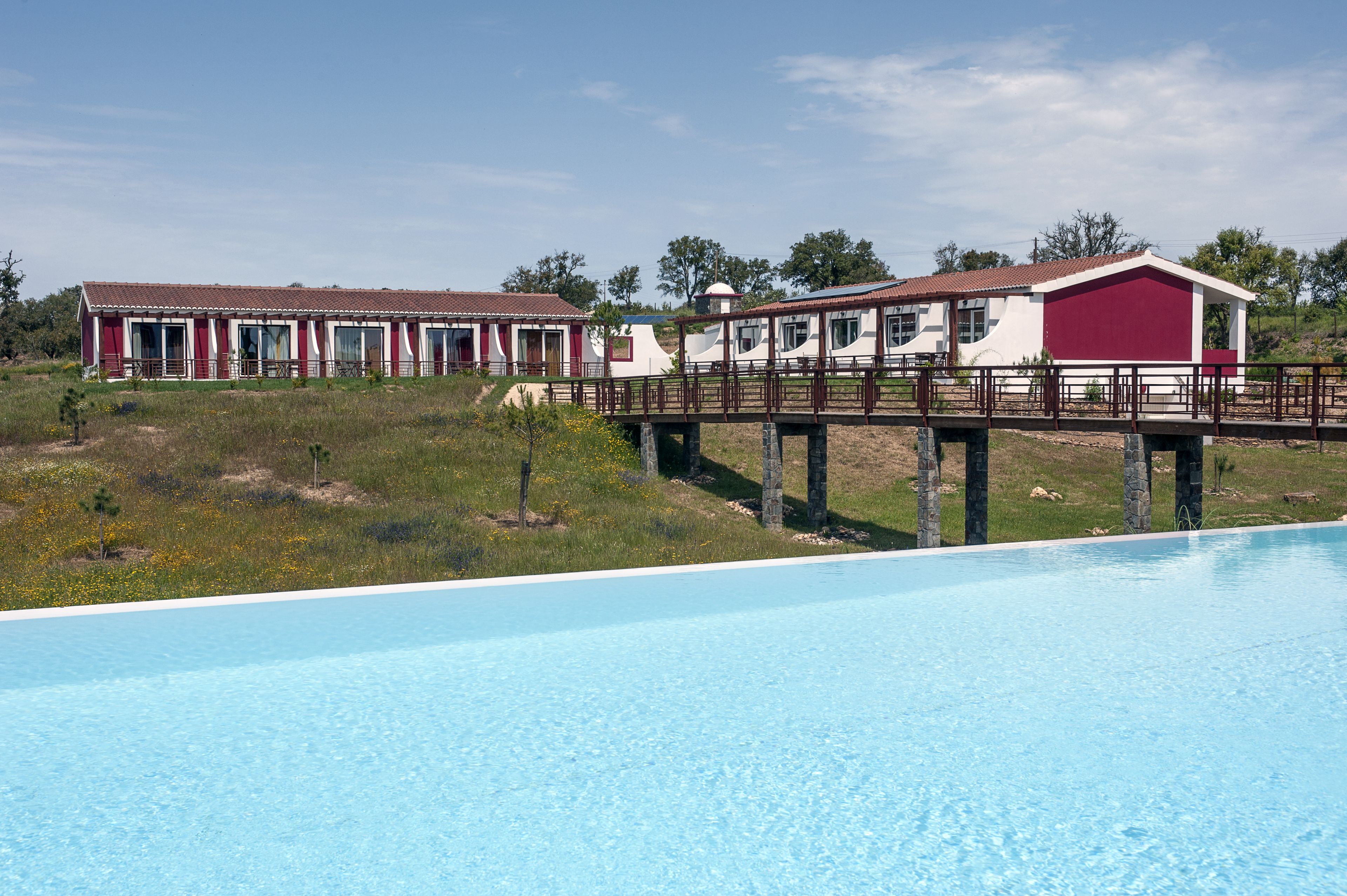 A pool with a wooden deck and a bridge connecting to a building with a red and white facade.