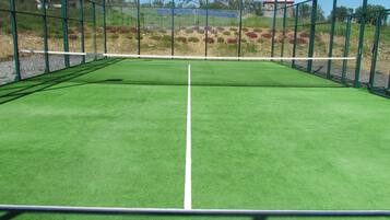 Una cancha de tenis con una red, rodeada por una valla verde.
