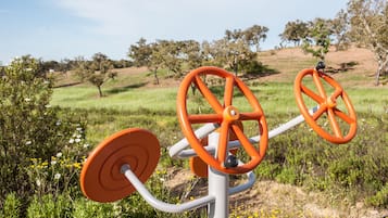 A stationary exercise machine in an outdoor setting with a grassy field and trees in the background.
