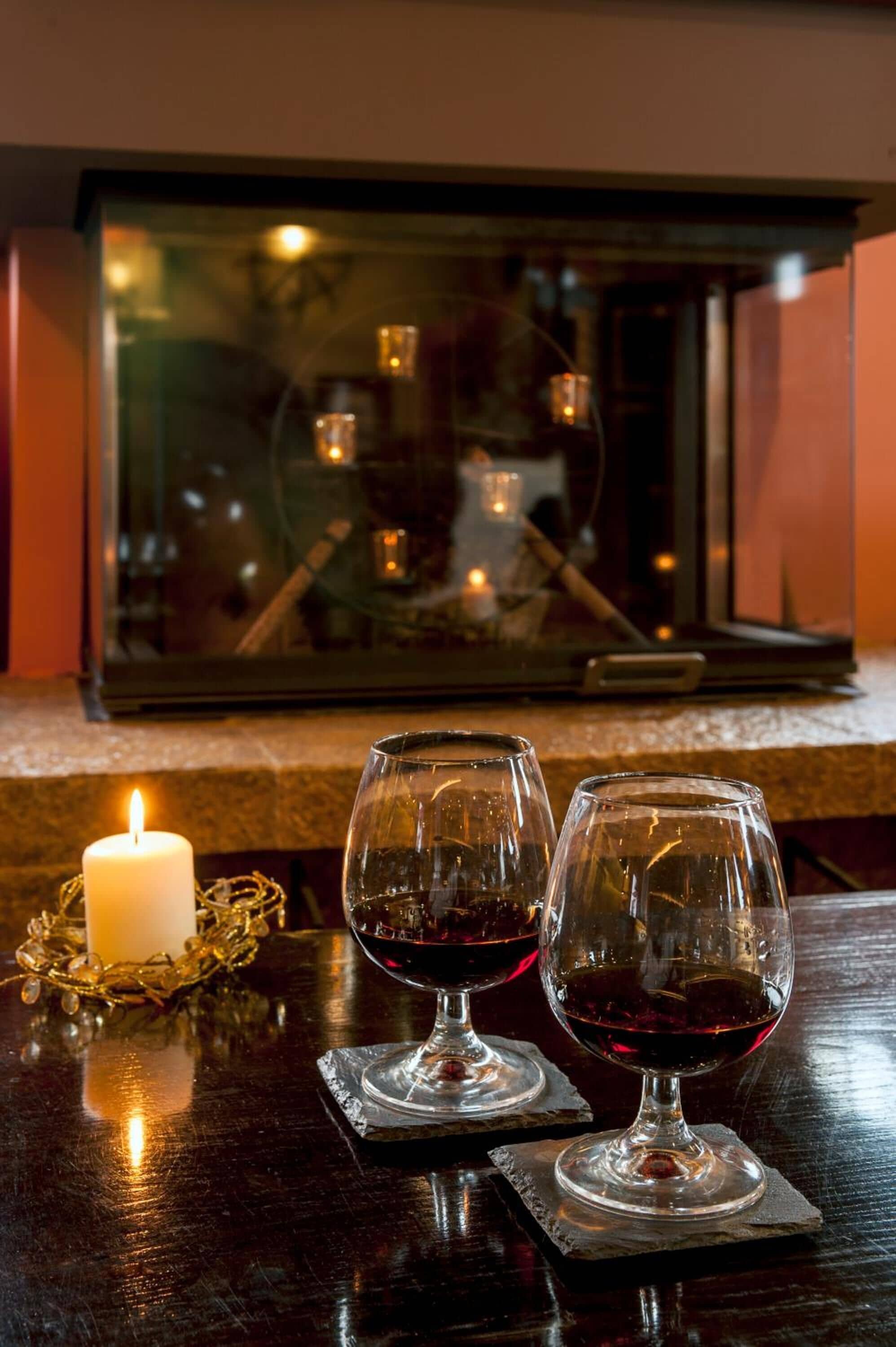 Uma vela, dois copos de vinho e uma mesa de vidro sobre uma superfície de madeira escura.