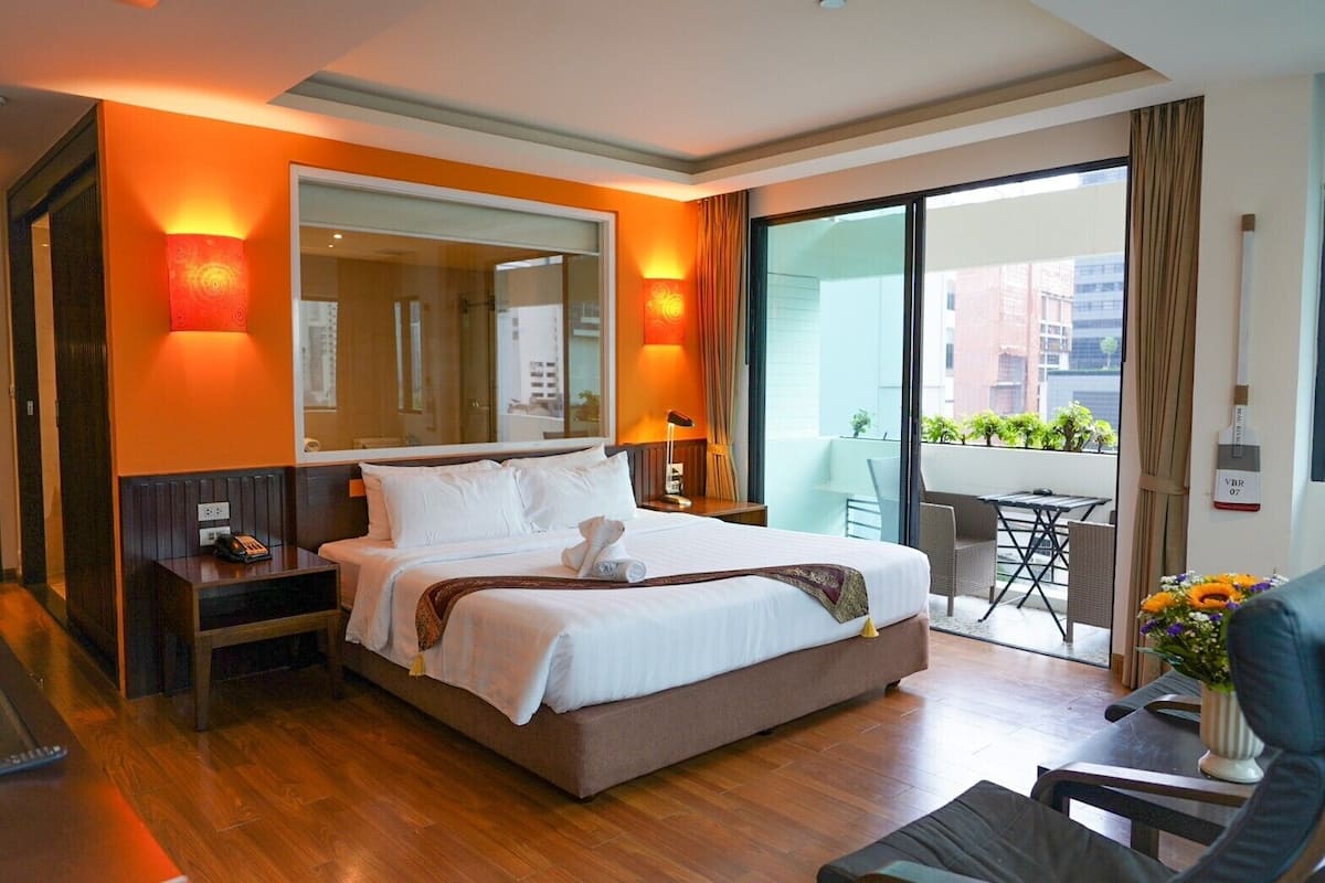 Ein Hotelzimmer mit einem großen Bett, einem Schreibtisch, einem Sessel sowie einem Balkon mit Tisch und Stühlen und einem großen Fenster.