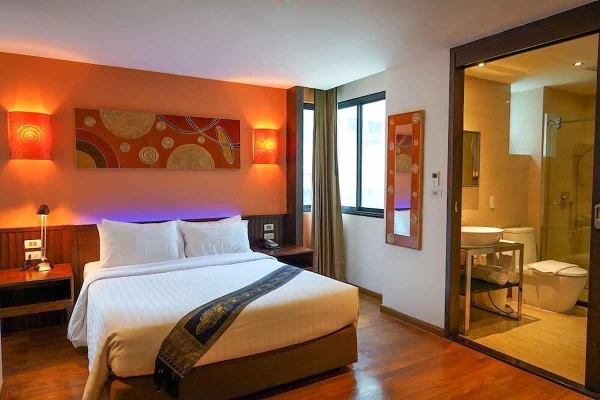Ein Hotelzimmer mit einem großen Bett, Nachttischen, einem Wandbild und einem Badezimmer mit Duschkabine und Spiegel.