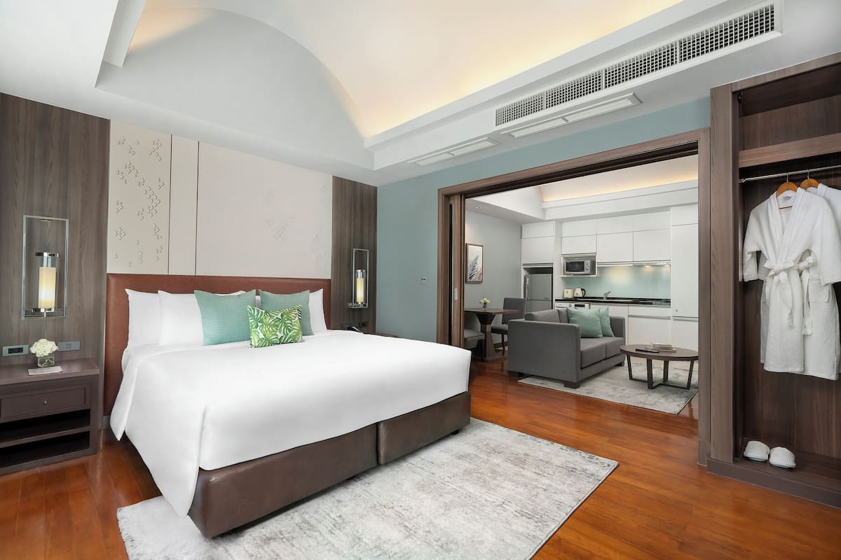 Ein modernes Hotelzimmer mit einem großen Bett, einer Sitzecke, einer Küchenzeile und einem durch eine offene Tür einsehbaren Badezimmer.