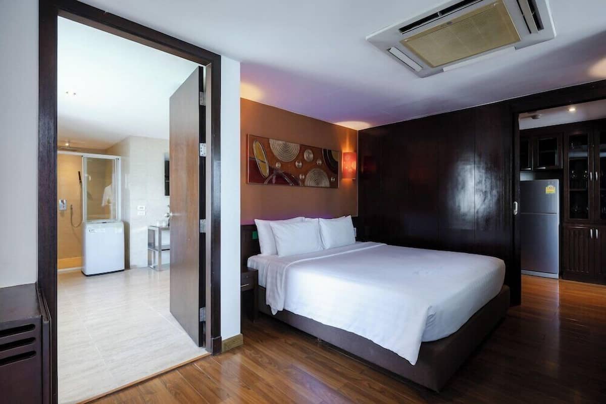 Ein modernes Hotelzimmer mit einem großen Bett, einer kleinen Küchenzeile und einem durchgegangene Tür sichtbar erkennbaren Badezimmer.