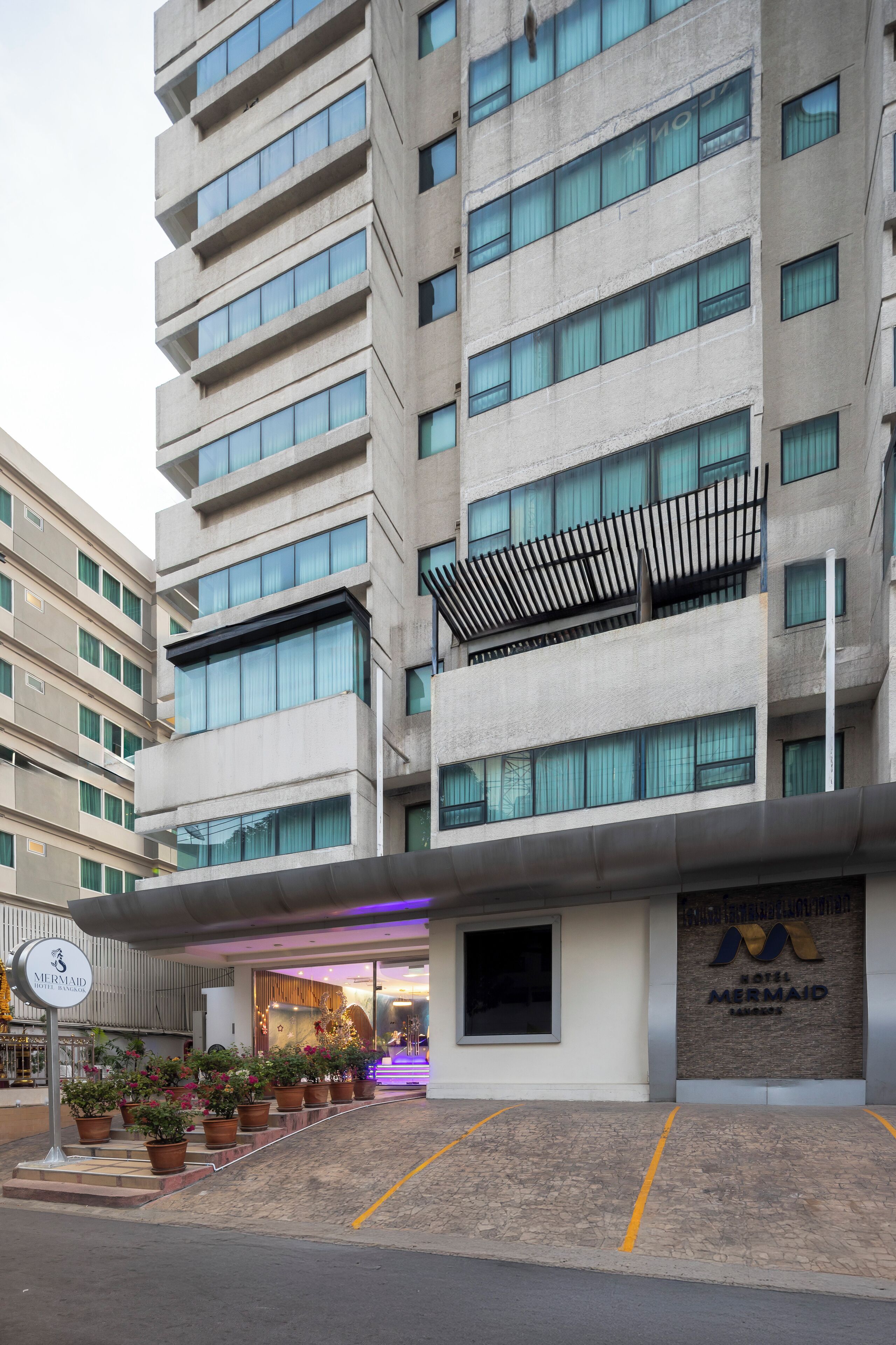 Un moderno edificio de hotel con fachada de concreto, varios balcones y un letrero que dice 'Hotel Mermaid'.