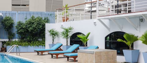 Un área de piscina con sillas de descanso, plantas en macetas y una escalera que lleva a una terraza superior.