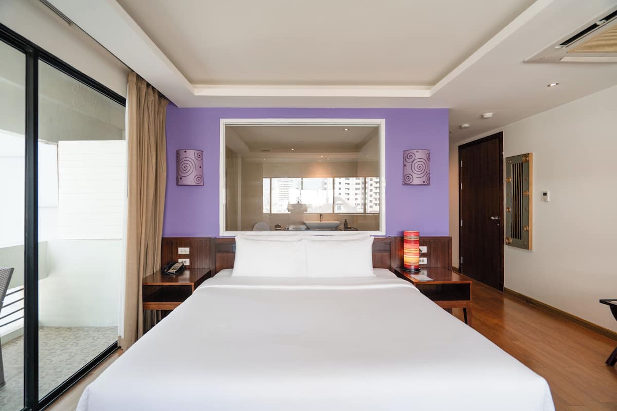 Ein Hotelzimmer mit einem großen Bett, einem Schreibtisch, einem Sessel, einem Spiegel und einem Fenster.